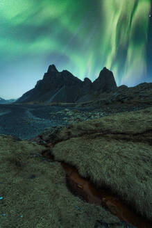 Erstaunliche Ansicht der grünen Aurora Borealis leuchtenden in den Nachthimmel über schneebedeckten Bergkamm mit schwarzem Sand Stockness Strand und Vestrahorn Berg im Hintergrund in Island - ADSF43661