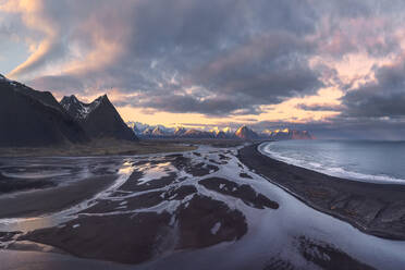 Weitwinkel majestätischen Blick auf felsigen Bergen mit Schnee bedeckt in der Nähe von gefrorenen See unter bewölktem Himmel Sonnenuntergang in Island - ADSF43679