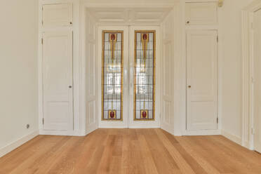 Interior design of light room with parquet floor and ornamental windows located between white cupboards - ADSF43697