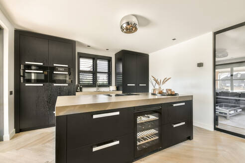 Inneneinrichtung einer modernen geräumigen Küche mit schwarzen Schränken, Arbeitsplatte mit eingebautem Weinkühler und Fischgrätenparkett - ADSF43714