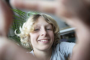 Happy blond boy looking through finger frame - NJAF00308