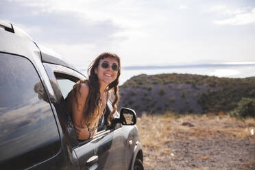 Happy young woman leaning out of car window - PCLF00309