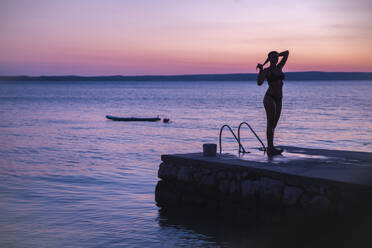 Silhouette einer Frau, die bei Sonnenuntergang auf einem Steg am Meer steht - PCLF00315