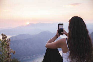 Young woman photographing sunset through smart phone - PCLF00321