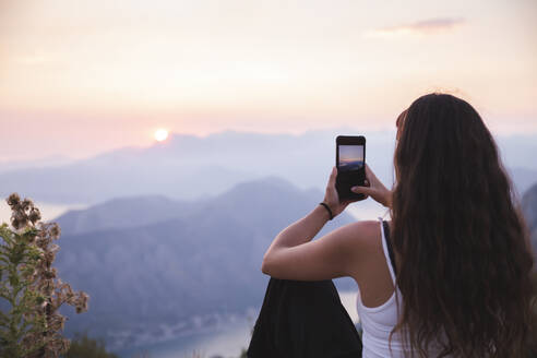 Junge Frau fotografiert Sonnenuntergang mit ihrem Smartphone - PCLF00321