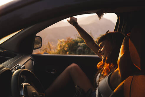 Glückliche junge Frau genießt im Auto bei Sonnenuntergang - PCLF00322