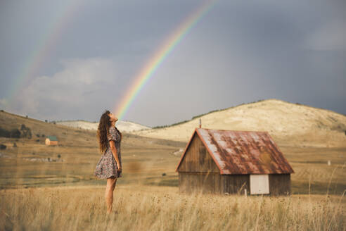 Junge Frau betrachtet den Regenbogen auf einer Wiese - PCLF00334