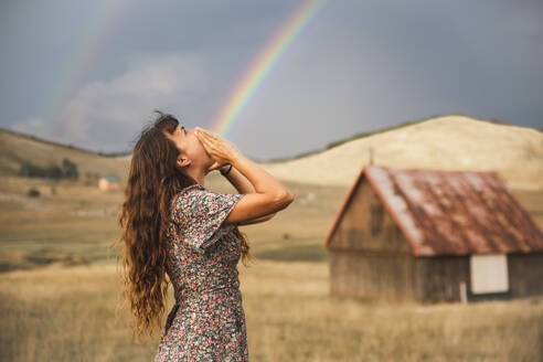 Optische Täuschung eines Regenbogens, der aus dem Mund einer im Feld stehenden Frau kommt - PCLF00335