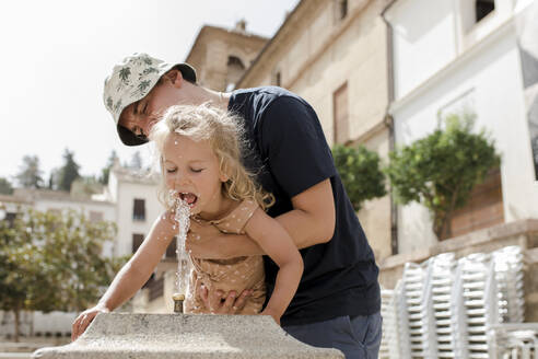Vater mit Tochter trinkt Wasser aus einem Brunnen - VIVF00468