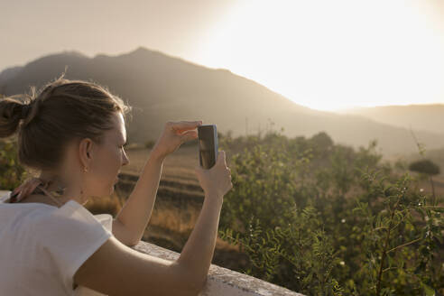Frau fotografiert bei Sonnenuntergang mit ihrem Smartphone - VIVF00472