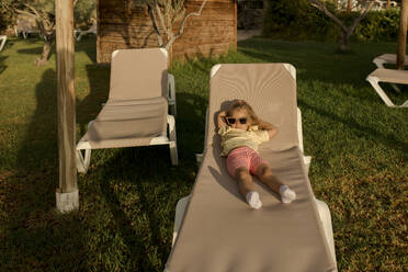 Cute girl wearing sunglasses lying on lounge chair - VIVF00494
