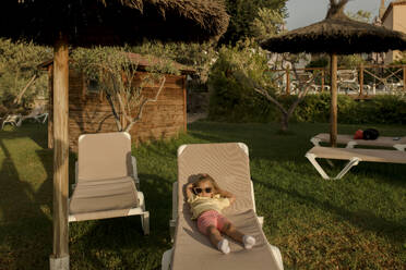Nettes Mädchen mit Sonnenbrille liegend und ruhend auf Liegestuhl im Resort - VIVF00495