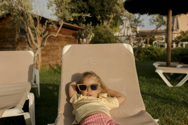 Girl wearing sunglasses lying on lounge chair - VIVF00496