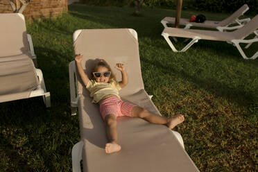 Cheerful girl relaxing and enjoying on lounge chair in resort - VIVF00499