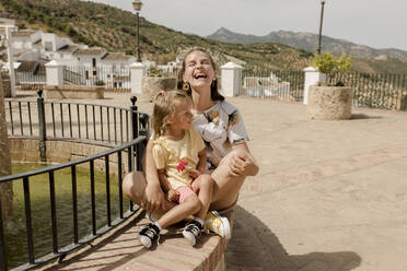 Cheerful mother and daughter sitting on sunny day - VIVF00516