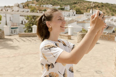 Glückliche junge Frau beim Fotografieren mit dem Handy an einem sonnigen Tag - VIVF00517