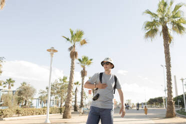 Man wearing hat standing at footpath - VIVF00537