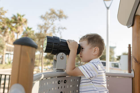 Junge schaut auf dem Spielplatz durch ein Teleskop - VIVF00544