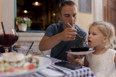 Man feeding shrimp to daughter in restaurant - VIVF00553