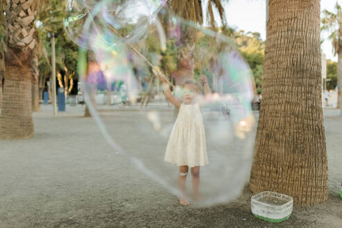 Girl playing with large soap bubble - VIVF00560