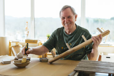 Smiling senior man paining wood in workshop - EBSF03086