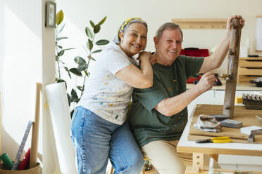 Glückliche ältere Frau mit Hand auf der Schulter eines Mannes, der in einer Werkstatt Holz lackiert - EBSF03088