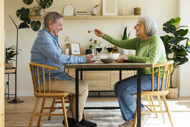 Happy woman feeding senior man at home - EBSF03094