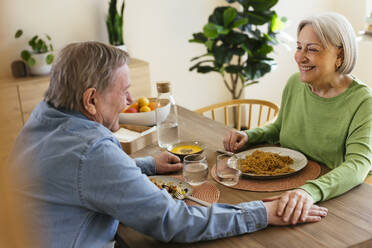 Glückliches älteres Paar mit gestapelten Händen beim Mittagessen zu Hause - EBSF03102
