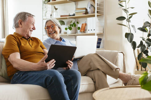 Glückliches älteres Paar sitzt mit Tablet-Computer auf dem Sofa im Wohnzimmer - EBSF03111