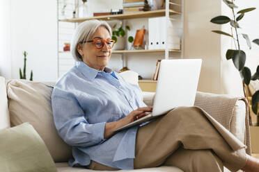 Ältere Frau mit Brille, die zu Hause einen Laptop benutzt - EBSF03112