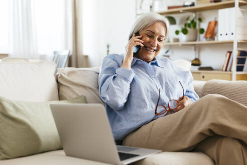 Glückliche ältere Frau, die zu Hause über ein Mobiltelefon spricht - EBSF03116