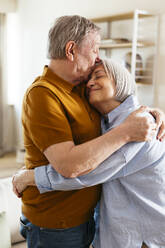 Senior man kissing on woman's forehead at home - EBSF03118