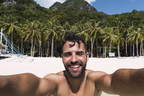 Ein fröhlicher Mann fängt einen Moment des Glücks ein, indem er ein Selfie an einem schönen Strand macht - PNAF05164