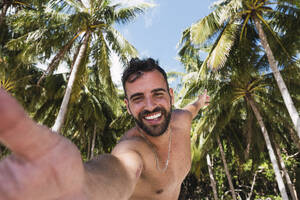 Ein fröhlicher Mann hält einen Moment mit üppigen tropischen Bäumen im Hintergrund fest, während er ein Selfie macht - PNAF05166