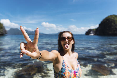 Happy young woman making peace sign in sea - PNAF05170