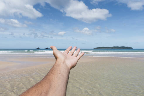Man's hand reaching towards sea at beach - PNAF05176