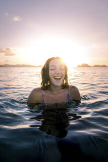 Glückliche Frau mit geschlossenen Augen schwimmt im Meer bei Sonnenuntergang - PNAF05180
