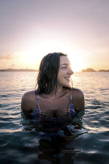 Lächelnde junge Frau hat Spaß im Wasser bei Sonnenuntergang - PNAF05185
