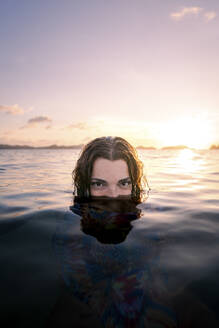 Woman hiding face in water at beach on sunset - PNAF05186