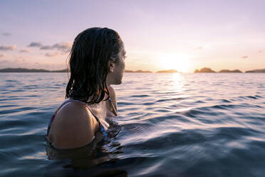 Frau schwimmt im Meer und schaut in die Sonne - PNAF05187