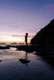 Silhouette einer Frau, die auf einem Felsen am Strand steht - PNAF05197