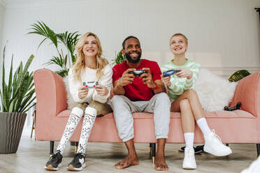 Glückliche Freunde spielen ein Videospiel auf dem Sofa im Wohnzimmer - MDOF00929