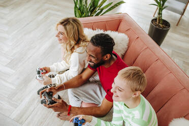 Freunde mit Spielcontroller spielen ein Videospiel auf dem Sofa sitzend zu Hause - MDOF00932