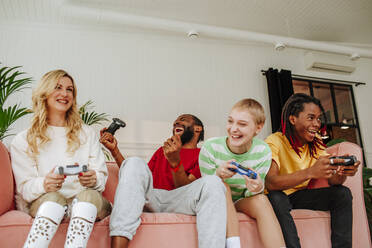 Aufgeregter junger Mann, der mit Freunden auf dem Sofa ein Videospiel spielt - MDOF00943
