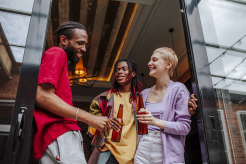 Fröhliche, gemischtrassige Freunde genießen ein Bier am Eingang einer Wohnung - MDOF00966