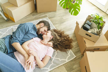 Zärtliches Paar, das auf dem Teppich neben Kartons in der neuen Wohnung liegt - OSF01495