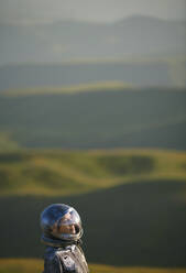 Contemplative woman wearing space helmet in front of landscape - AZF00500