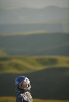 Kontemplative Frau mit Weltraumhelm vor einer Landschaft - AZF00500