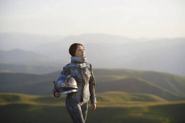 Kontemplative Frau mit Weltraumhelm in einer Landschaft stehend - AZF00504