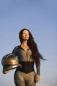Frau mit langen Haaren hält Weltraumhelm unter blauem Himmel - AZF00505